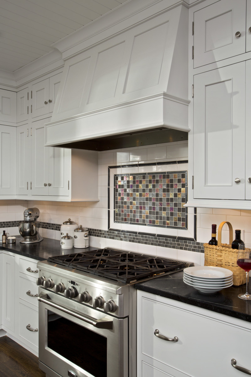 A simple case that mirrors the custom cabinets helps this hood blend in, drawing the eye to the mosaic backsplash. By Teakwood Builders, kitchen and bath remodeler, custom home builder and general contractor Saratoga Springs and Capital Region.