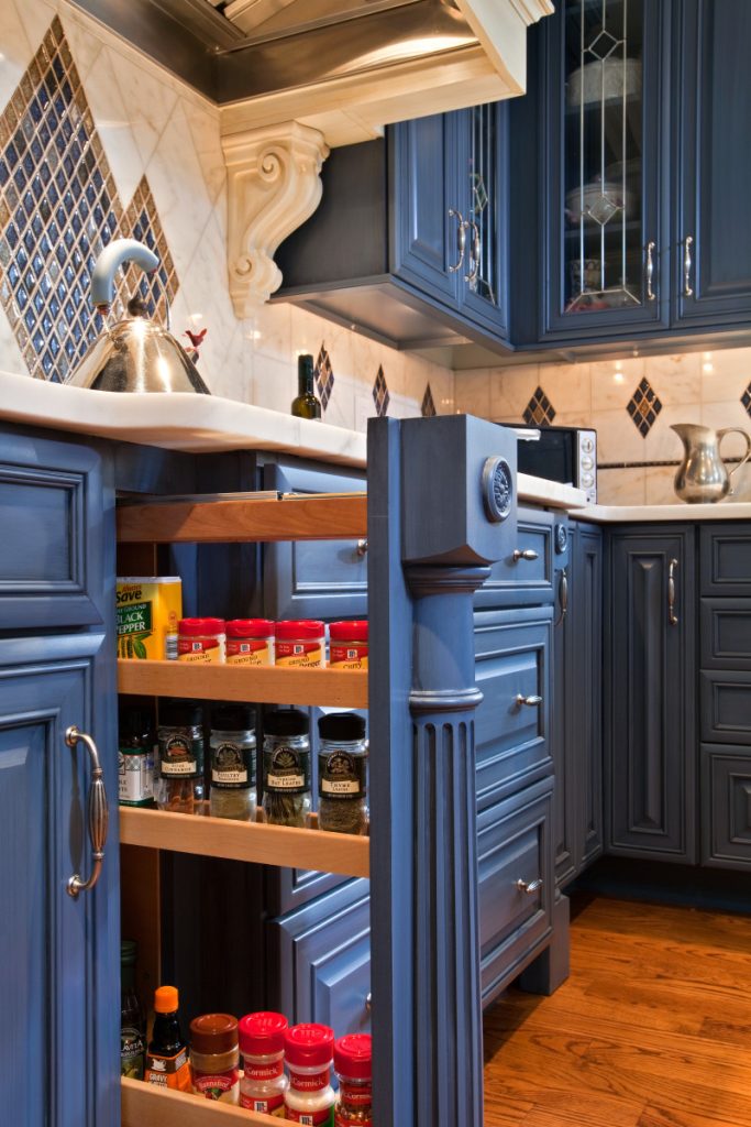 Custom millwork in this Saratoga Springs, NY, kitchen design keeps spices handy with a pullout rack that neatly disappears when not in use.