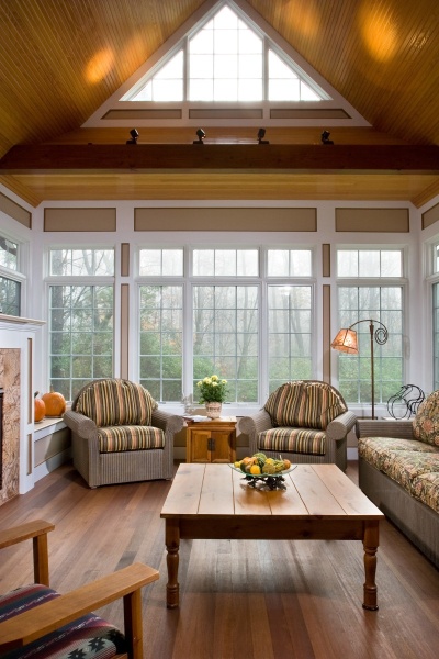 The vaulted ceiling Teakwood Builders installed in this year-round sunroom features Douglas fir beadboard, while the floor is of rich mahogany. Detailed wall paneling mimics the architectural elements used on the exterior of this addition. A made-to-measure bench adjacent to the gas fireplace is hinged for discreet storage.