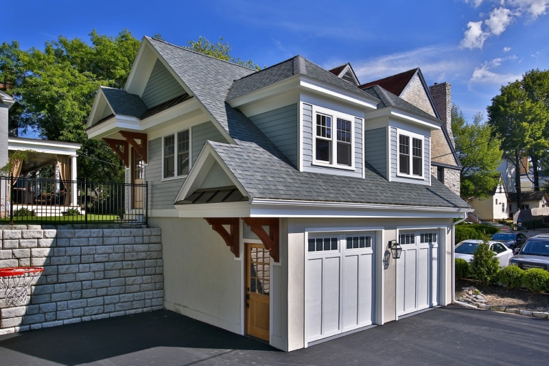 A stone retaining wall made it possible for Teakwood Builders to create a multilevel two-car garage with room for a guest apartment upstairs. Timber brackets, a natural wood door, cedar siding and stucco bring the carriage house into historical concert with the home without directly mimicking the older materials.