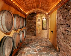 A unique barrel-vaulted ceiling is illuminated by low-voltage accent lighting, concealed by tailored molding. Teakwood Builders repurposed wine casks as part of a decorative wall display wine cellar wall treatment.