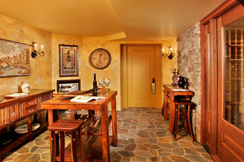 A tasting room features cultured stone walls, natural slate floors, wrought-iron candle wall sconces and solid wood doors with hand-milled trims in Teakwood Builders' transformation of a Loudonville, NY, basement into a Tuscan wine cellar.